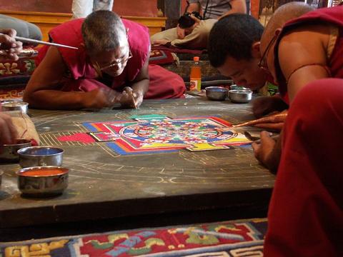 Groep monniken die een mandala van gekleurd zand aan het maken is.